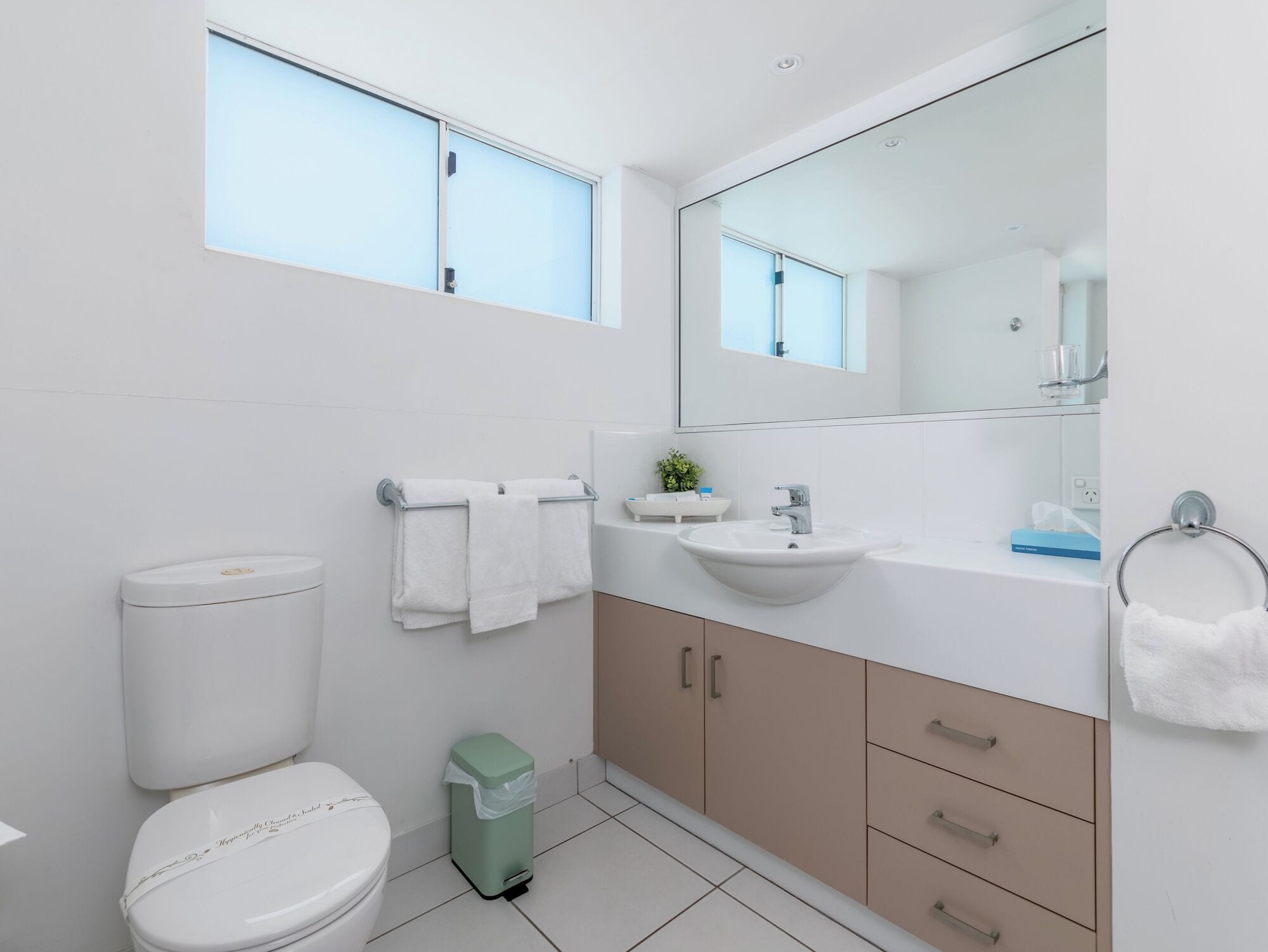 A modern bathroom with a toilet, sink, mirror, and cabinets.