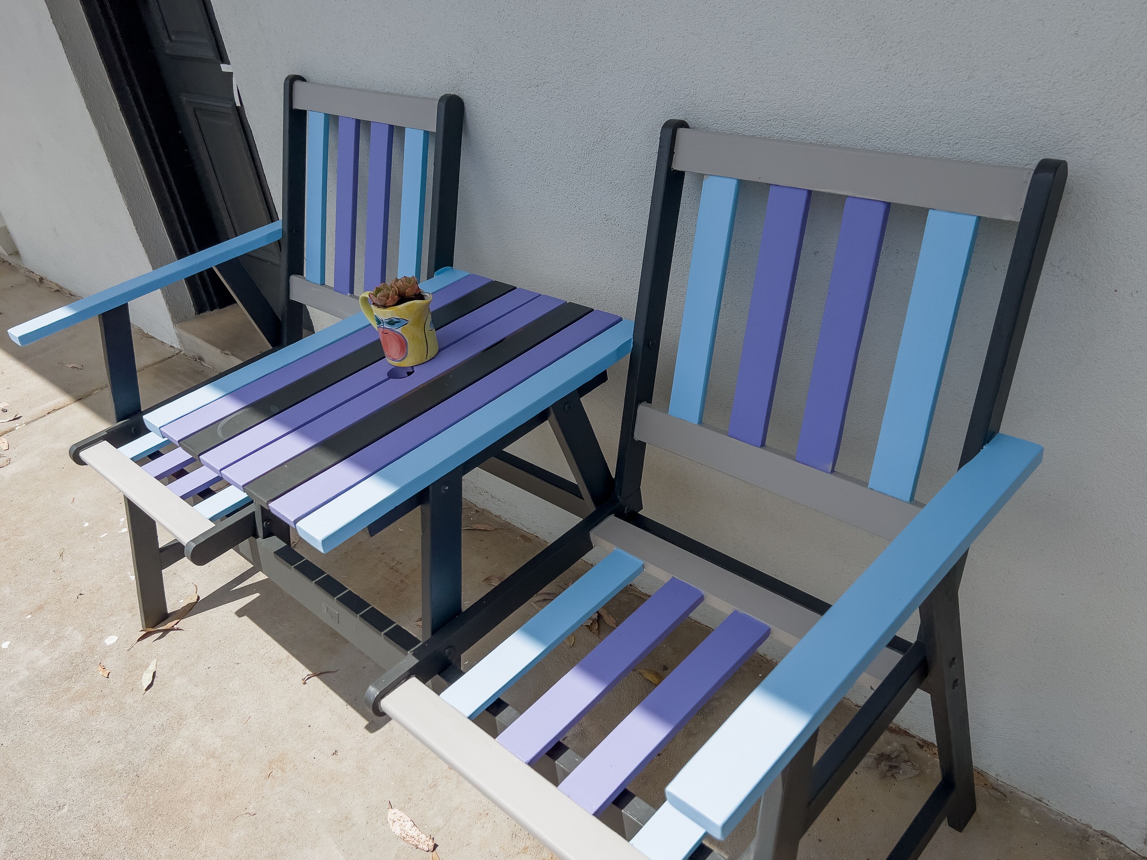 Dos sillas con diseño a rayas, una mesita pequeña y un objeto decorativo sobre la mesa.