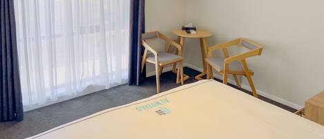 A hotel room with a bed, two wooden chairs, a small table, a TV on the wall, and a painting.