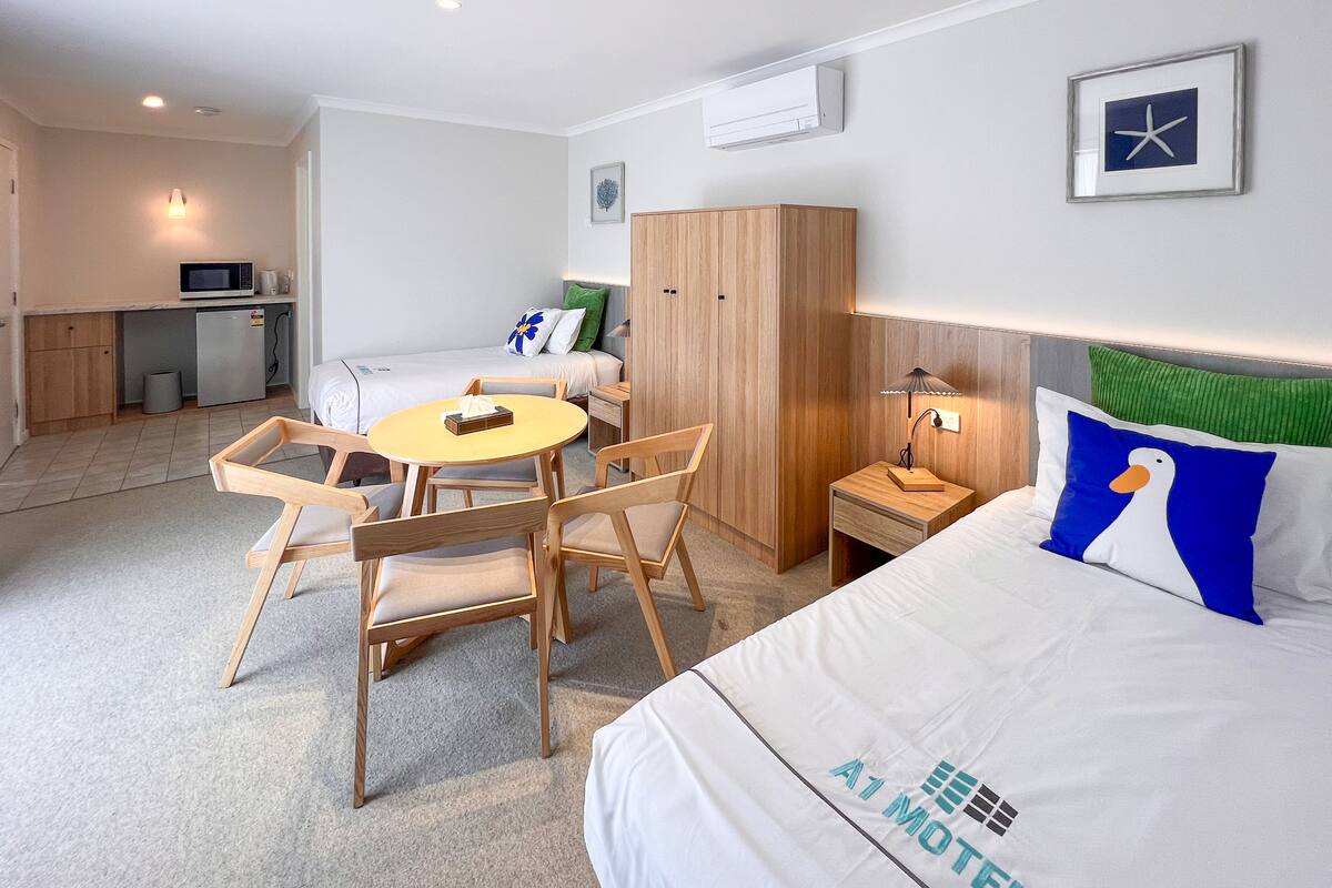 A hotel room with a bed, a desk, a chair, a small table, and a microwave.
