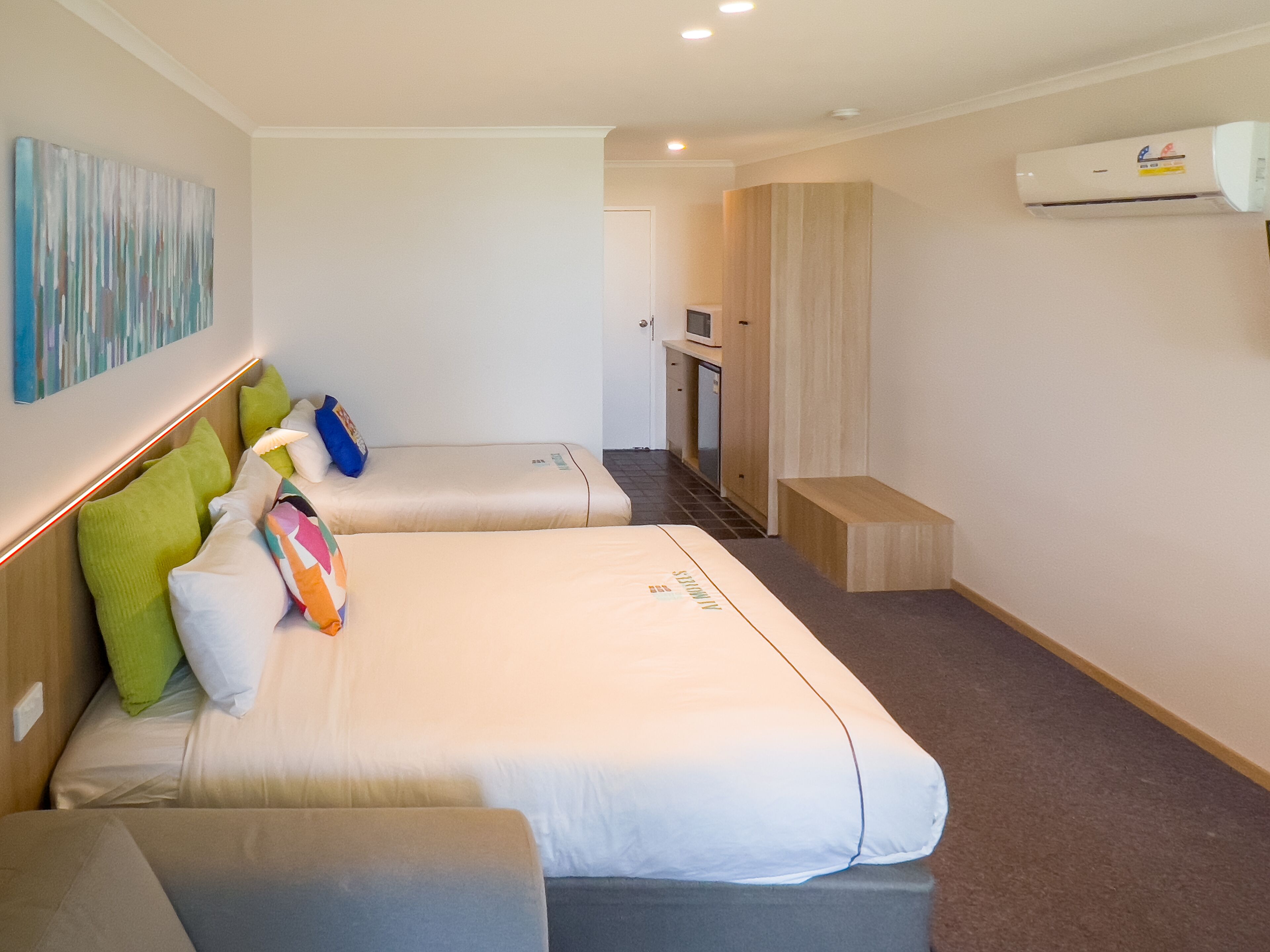 Una habitación de hotel con dos camas, un kitchenette pequeño y un baño.