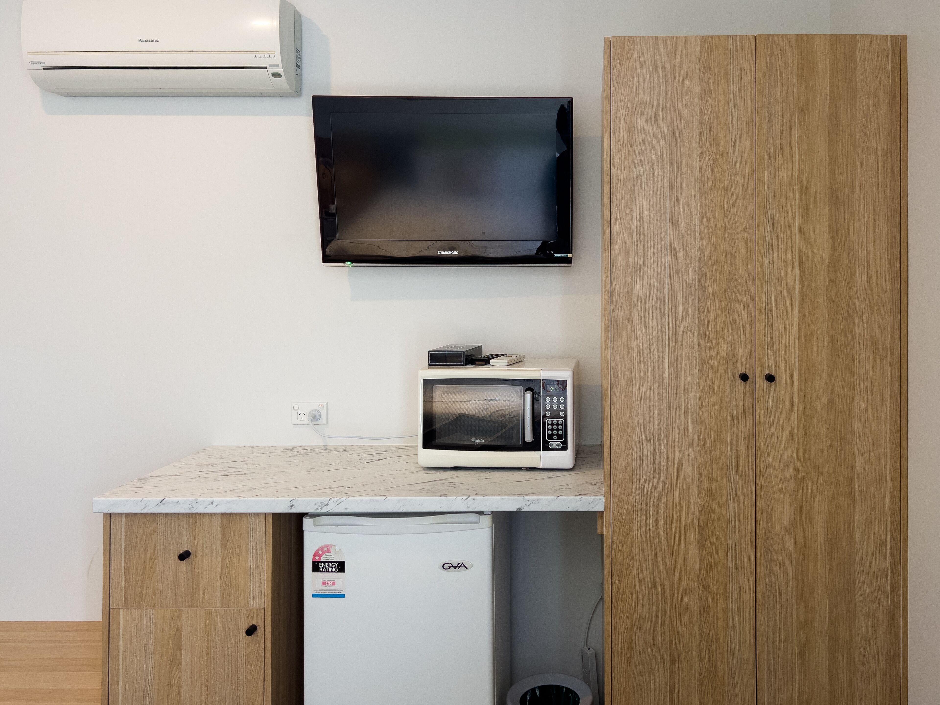 A kitchenette with a microwave, a small refrigerator, and a wall-mounted air conditioner.