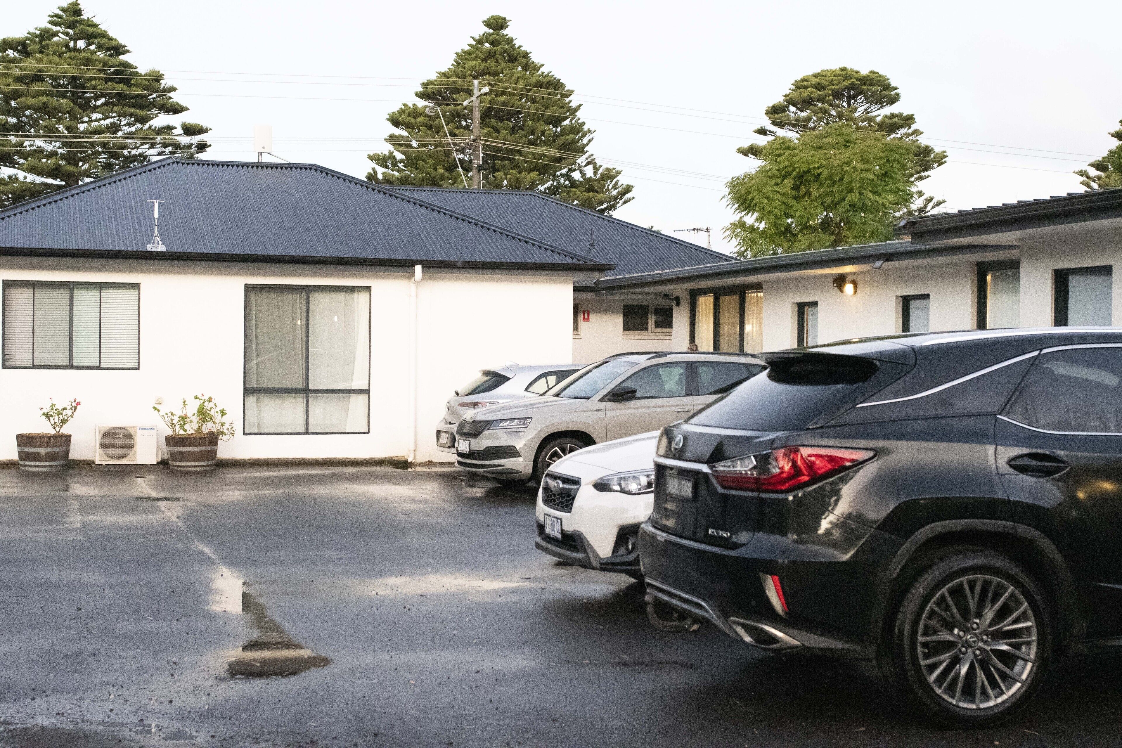 A parking lot with several cars parked in front of a building with a dark roof and white walls.