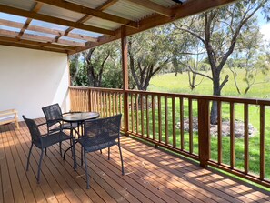 A wooden deck with a table and chairs, overlooking a grassy area with trees.