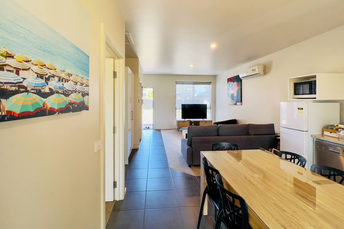 A modern apartment with a dining area, kitchen, living room, and a hallway leading to a balcony.