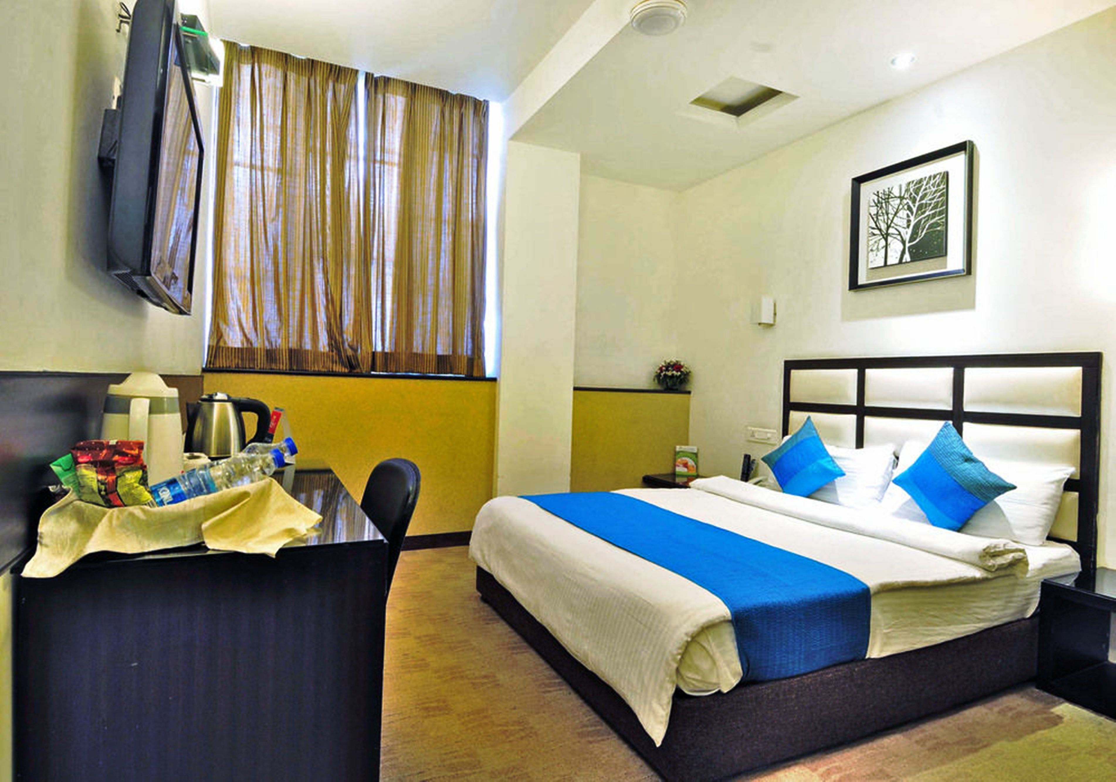 A hotel room with a bed, a desk, a chair, a television, and a window with curtains.