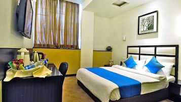 A hotel room with a bed, a desk, a chair, a television, and a window with curtains.