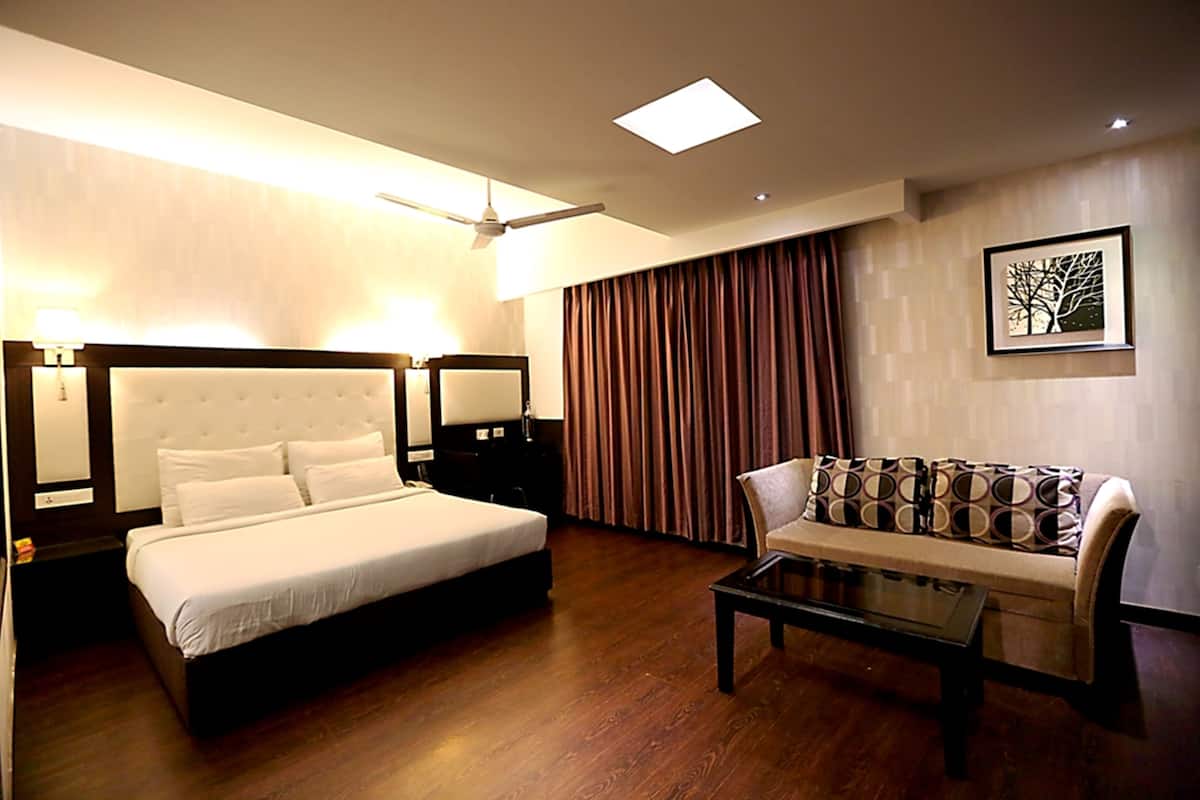 A hotel room with a large bed, a sofa, a coffee table, a ceiling fan, and a framed picture on the wall.