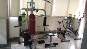 Un gimnasio con diversos equipos de ejercicio, incluyendo un banco de pesas rojo, una bicicleta estática y una cinta de correr.