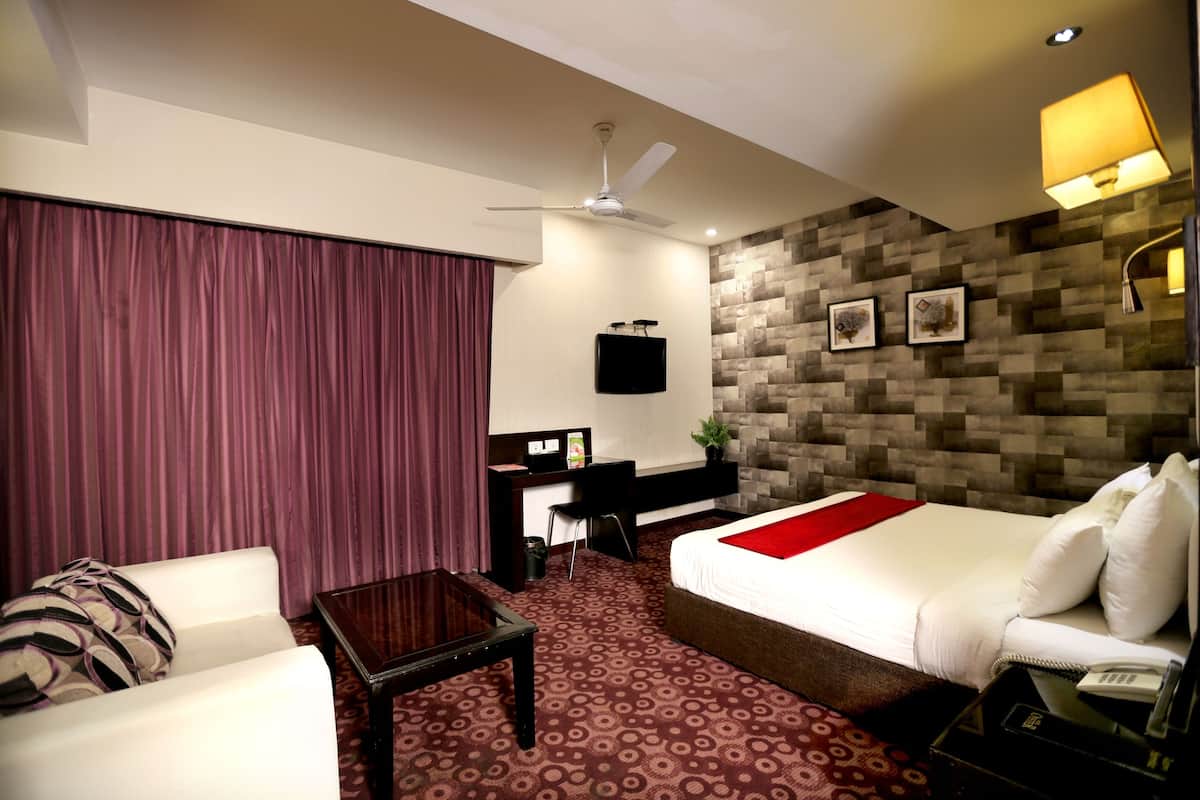 A hotel room with a bed, a desk, a chair, a coffee table, and a ceiling fan.