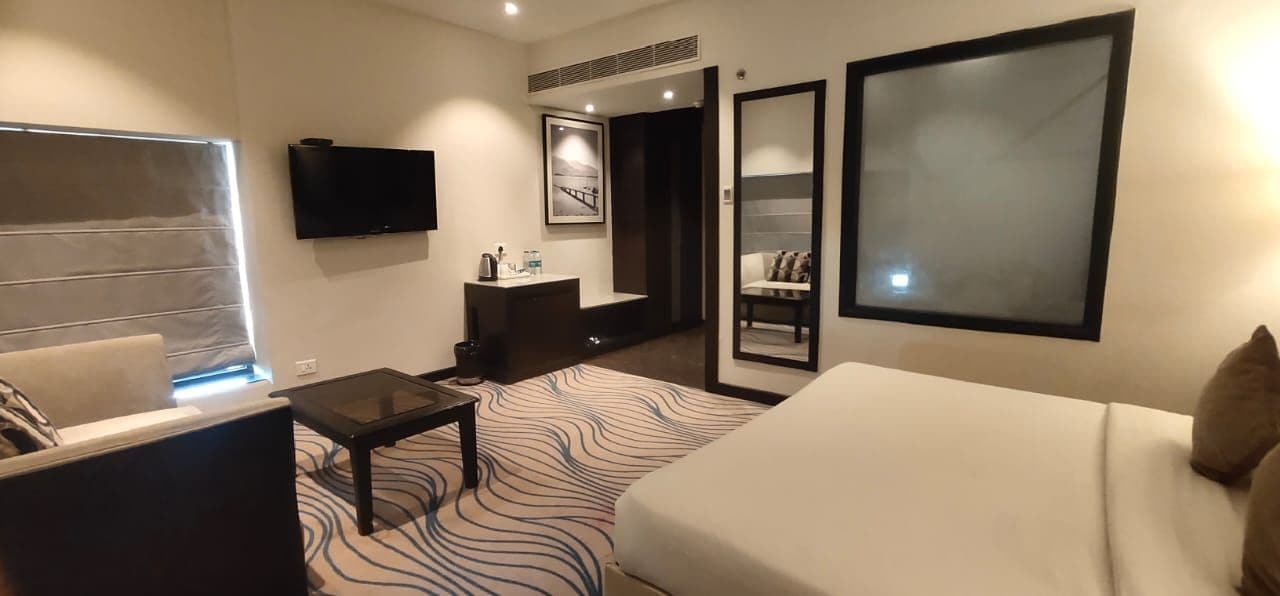 Ein Hotelzimmer mit Bett, Sofa, Schreibtisch, Fernseher, Badezimmer und einem großen Spiegel.