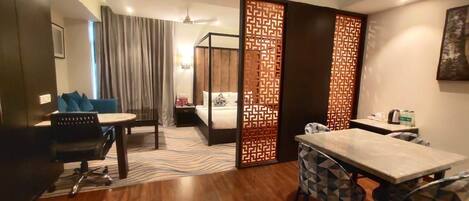 Habitación de hotel con cama, escritorio, silla, mesa de comedor y un separador decorado con un diseño geométrico.