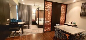 A hotel room with a bed, a desk, a chair, a dining table, and a partition with a geometric pattern. - Hotel Oyster (Chandigarh)