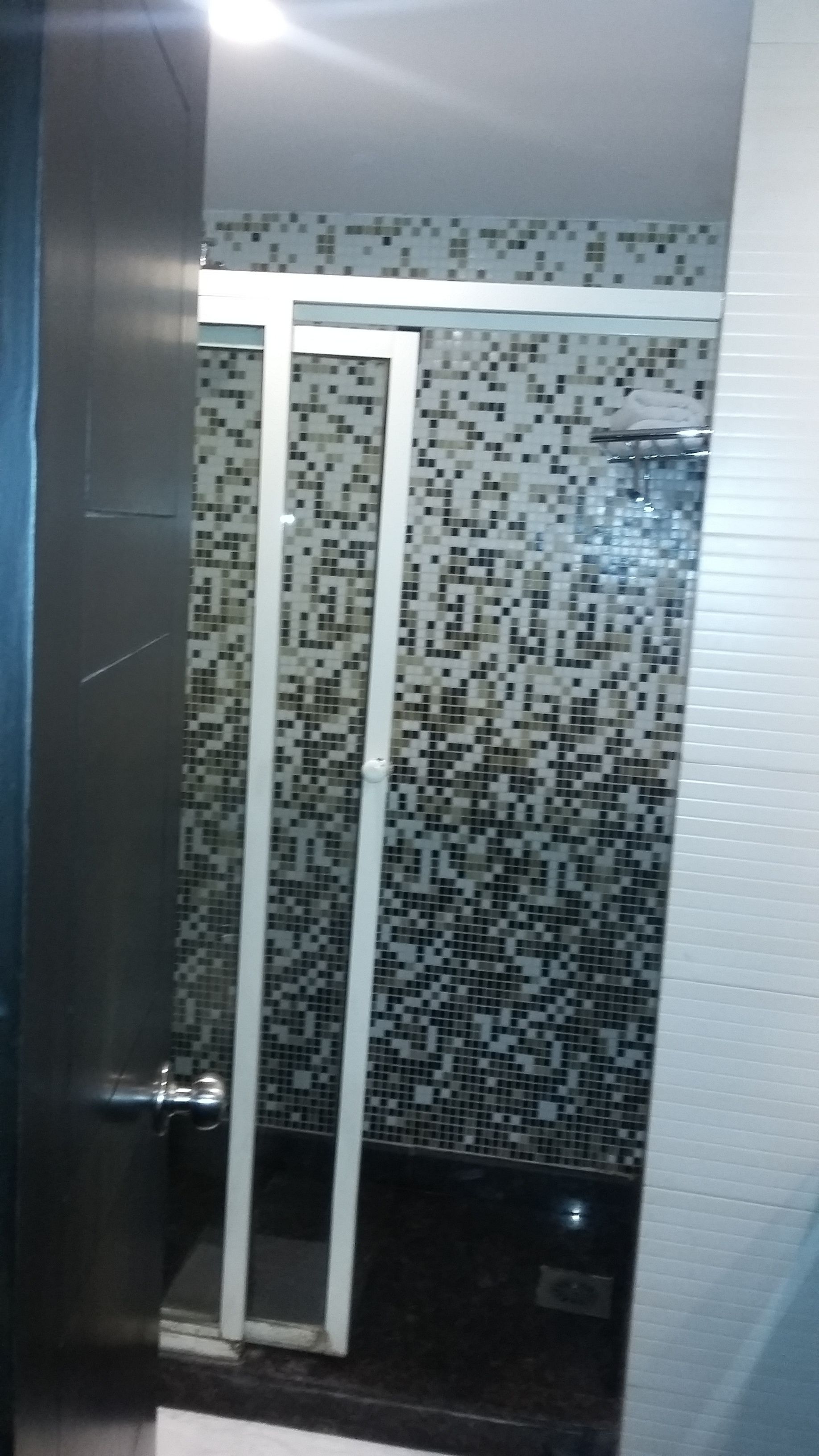 A bathroom with a tiled wall, a glass shower enclosure, and a door.