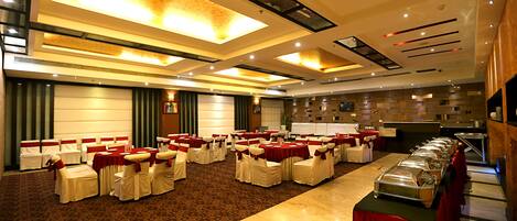 Une salle de banquet avec des rangées de tables et de chaises, un buffet et un grand plafond illuminé.