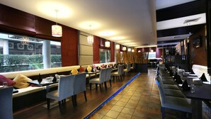 A restaurant with long communal tables, cushioned seating, and pendant lighting. - Hotel Oyster (Chandigarh)