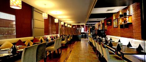 Een restaurant met lange gedeelde tafels, zitjes en hangende hanglampen.