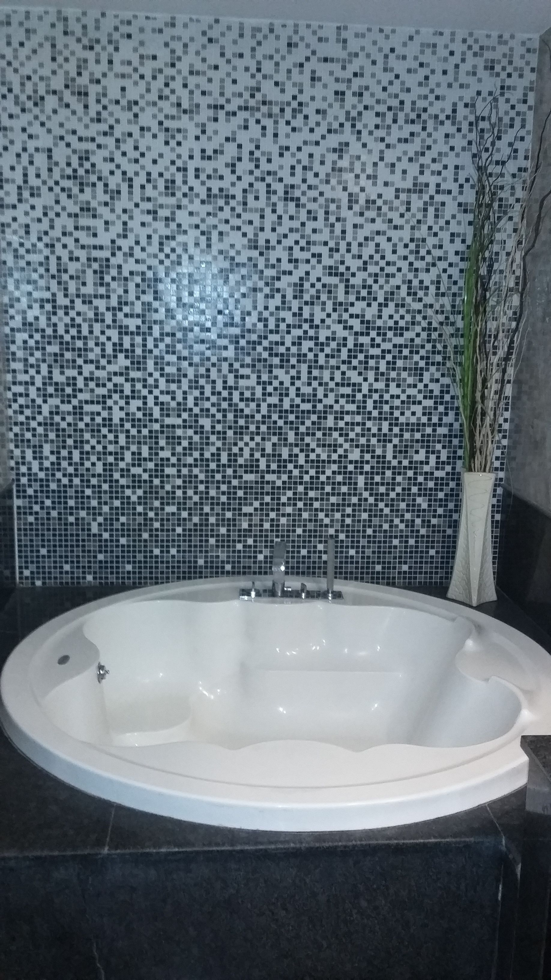 A bathroom with a freestanding bathtub, a tiled mosaic wall, and a potted plant.