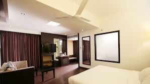 A hotel room with a bed, a desk, a chair, a TV, and a ceiling fan. - Hotel Oyster (Chandigarh)