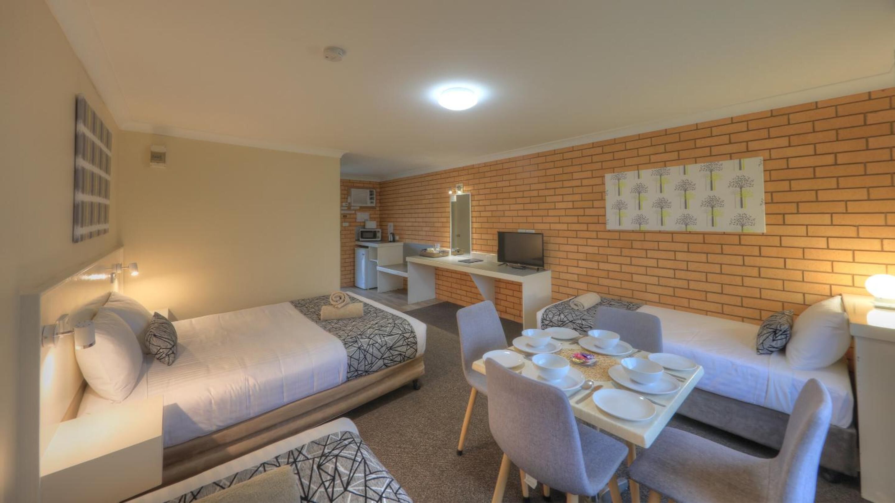 A hotel room with two single beds, a dining table with chairs, a small kitchenette, and a TV.