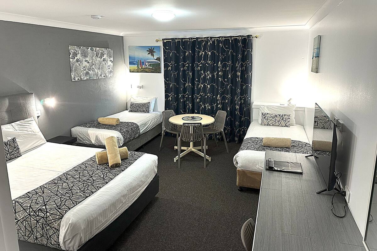 Ein Hotelzimmer mit zwei Einzelbetten, einem kleinen runden Tisch mit Stühlen, einem Schreibtisch und einem Sessel sowie einem großen Spiegel.