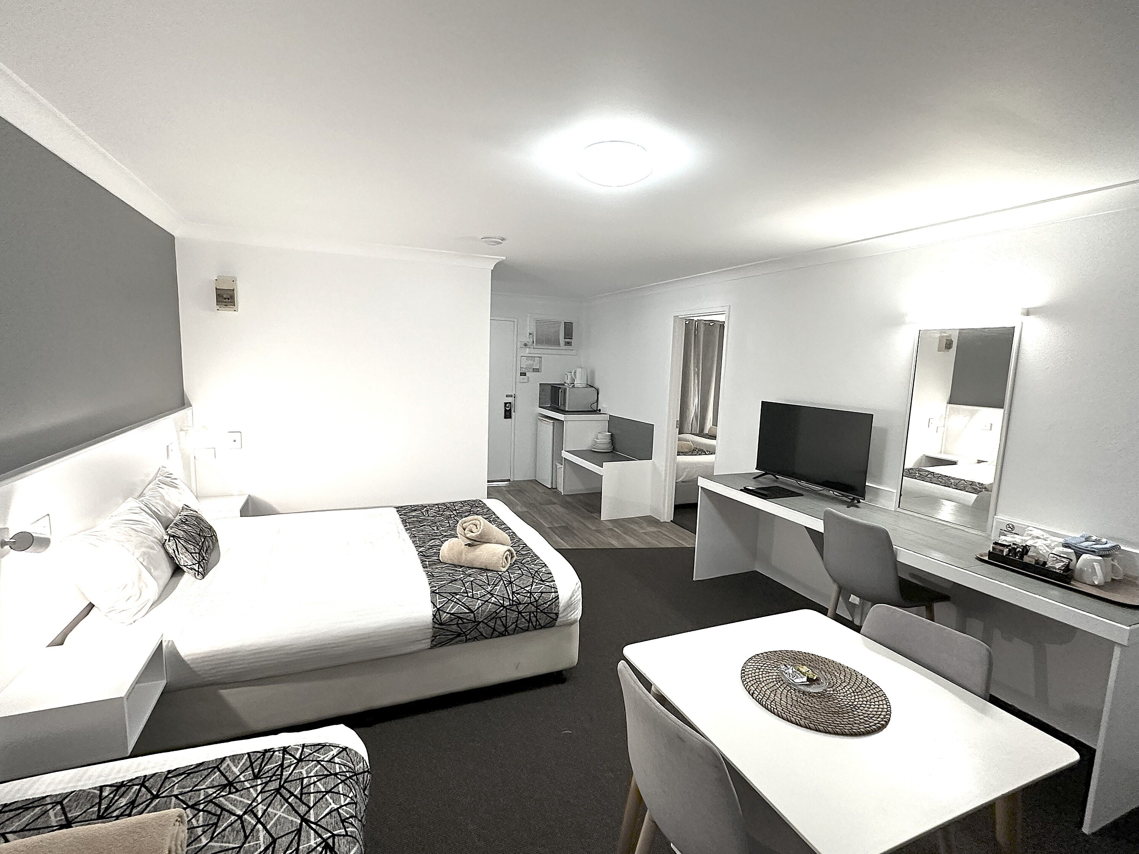 A hotel room with a bed, a desk, a TV, and a dining area.