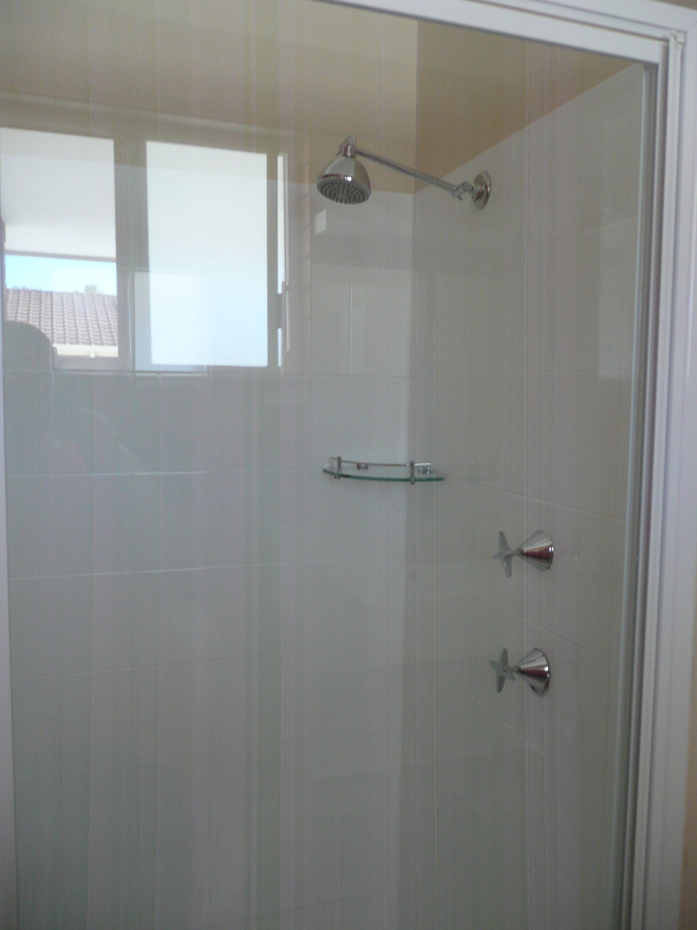 A glass-enclosed shower with a handheld showerhead and a handheld shower attachment.