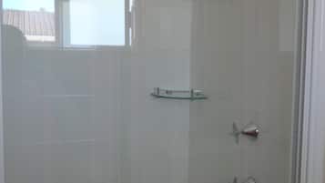 A glass-enclosed shower with a handheld showerhead and a handheld shower attachment.