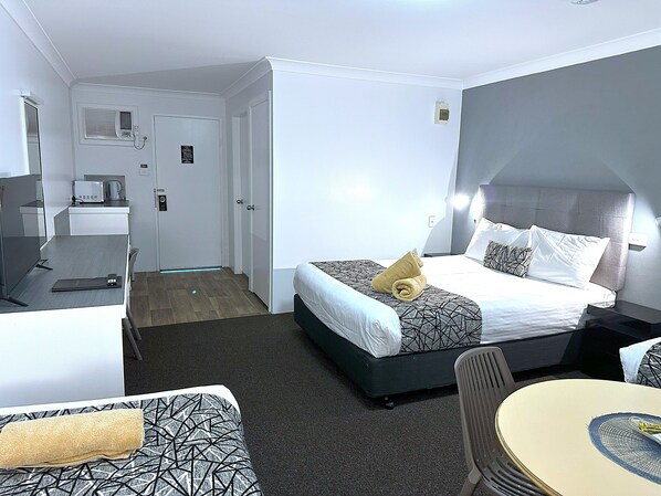 A hotel room with a bed, a desk, a chair, and a small table. - Rosebourne Gardens Motel (Woolgoolga)
