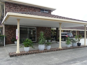 A building with a covered entrance, potted plants, and a speed limit sign. - Rosebourne Gardens Motel (Woolgoolga)