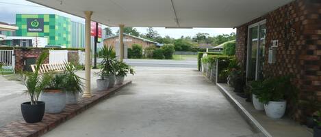 A covered walkway leading to a building with a brick facade, potted plants, and a sign for Woolworths.