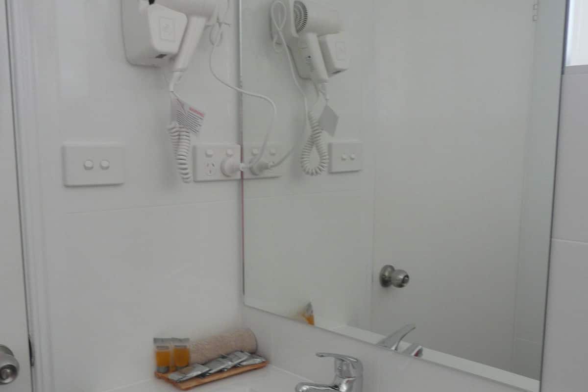 Ein Badezimmer mit einem weißen Waschbecken, einem Spiegel und zwei an der Wand befestigten Haartrocknern.