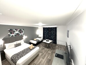 A compact hotel room with a large bed, a smaller bed, a desk, and a TV. - Rosebourne Gardens Motel (Woolgoolga)
