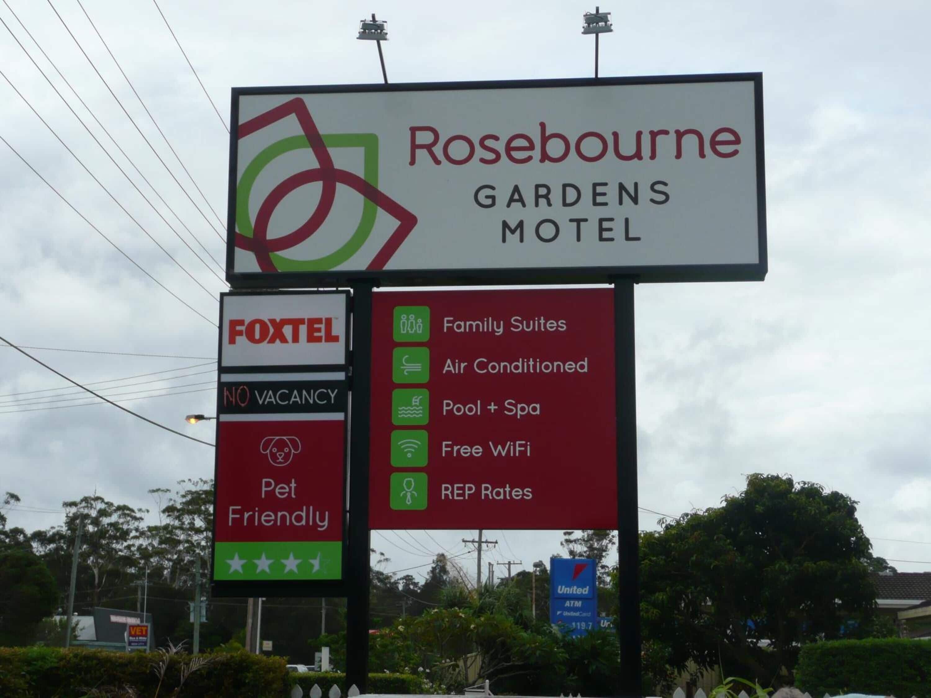 Un panneau indiquant le « Rosebourne Gardens Motel », avec des équipements tels que des suites familiales, la climatisation, une piscine et un spa, une connexion Wi-Fi gratuite et une politique d’acceptation des animaux de compagnie.