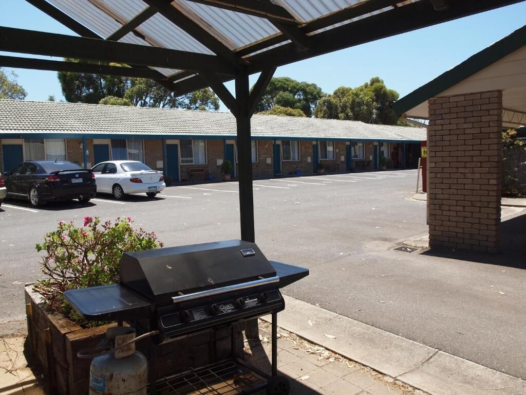 Een overdekt buitengebied met een barbecuegrill, een bakstenen gebouw en een rij motelkamers op de achtergrond.
