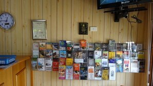 A room with a wooden wall, a clock, a television mounted on the wall, and a collection of books and magazines displayed on the wall. - Peppinella Motel (Delacombe)