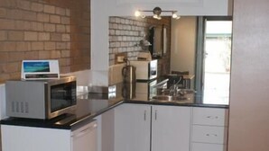 A compact kitchen with white cabinets, a microwave, and a coffee machine. - Peppinella Motel (Delacombe)