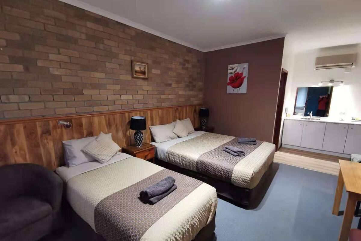 Ein Hotelzimmer mit zwei Betten, einem Holz-Kopfteil, einer Ziegelwand, einem Gemälde, einem Spiegel und einer Küchenzeile.