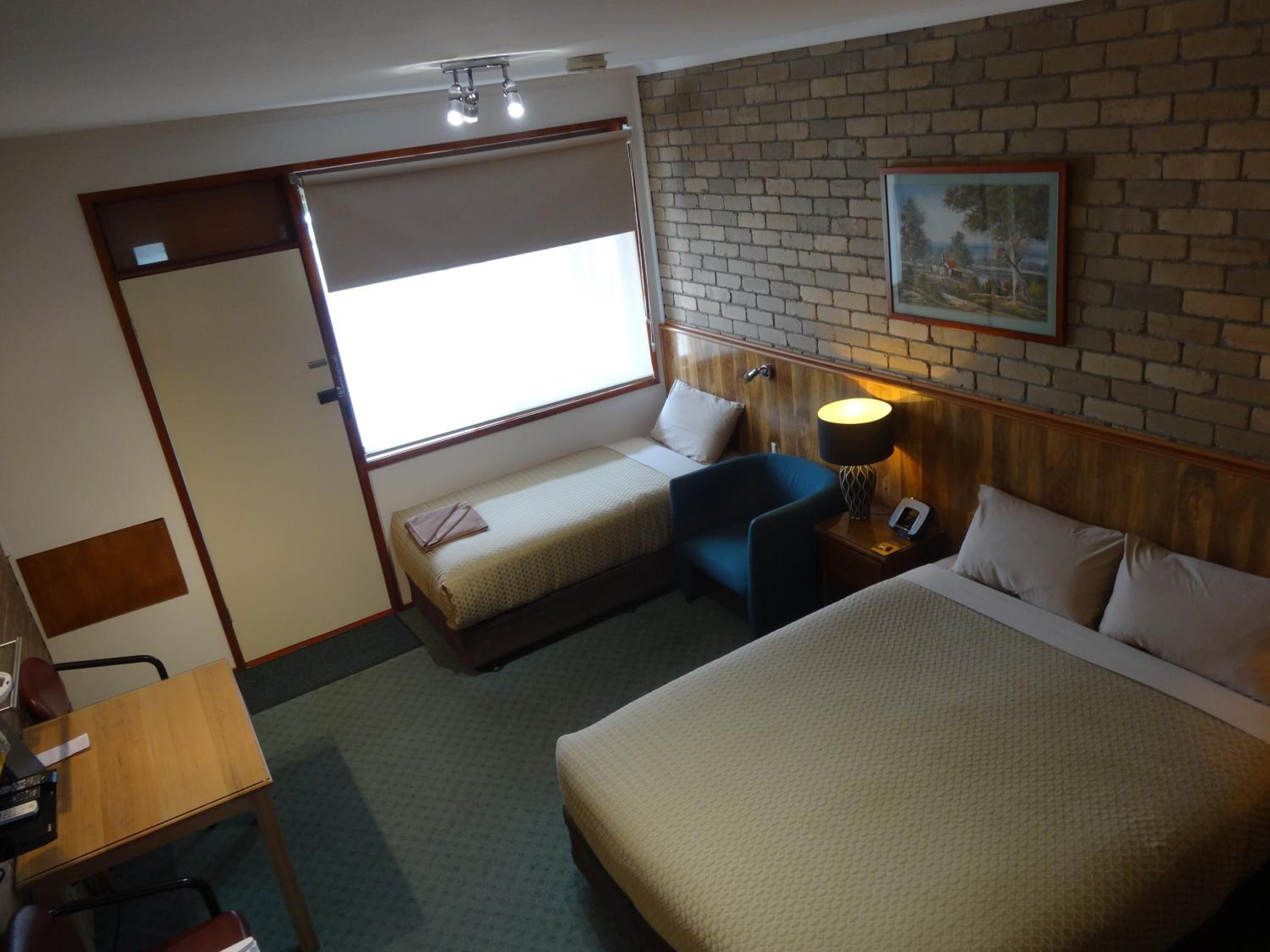 A hotel room with two beds, a desk, a chair, a lamp, and a painting on the wall.