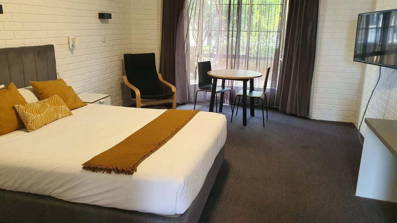 A hotel room with a large bed, a desk, a chair, and a TV.