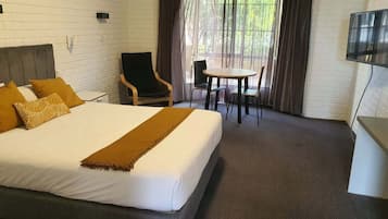A hotel room with a large bed, a desk, a chair, and a TV.