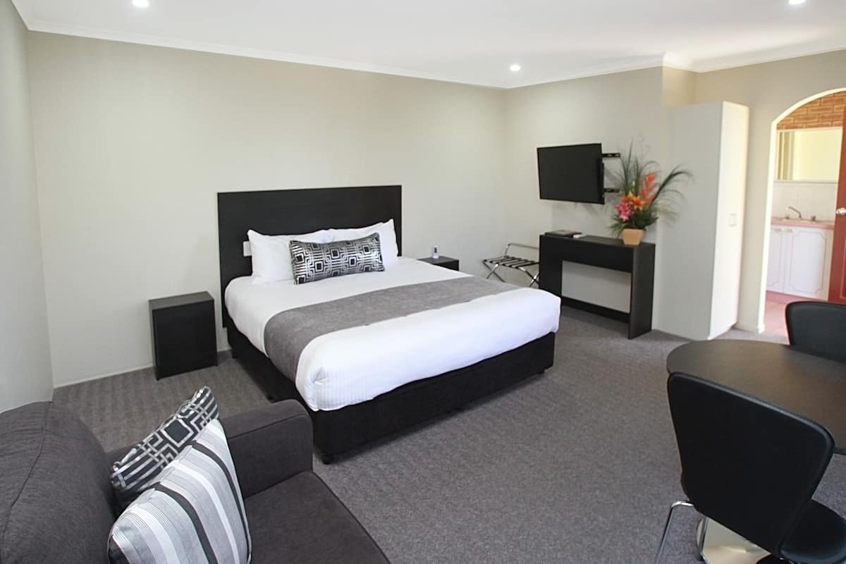 A modern hotel room with a large bed, a desk with a flat-screen TV, a seating area with a couch, and a small kitchenette.