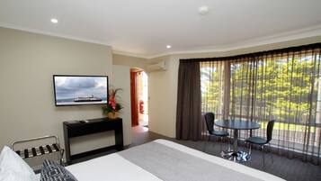 Une chambre d’hôtel comprenant un lit, un téléviseur fixé au mur, un bureau avec une chaise, une petite table avec des chaises et une grande fenêtre avec des rideaux.