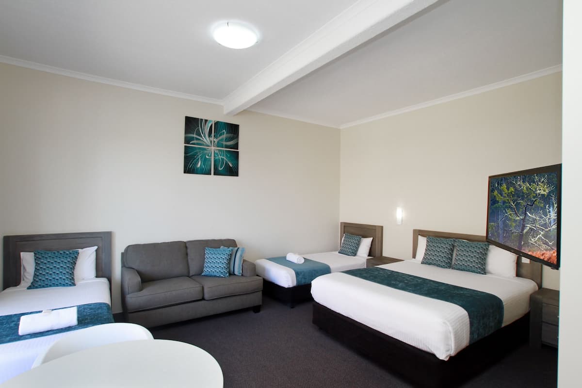 A hotel room with two single beds, a sofa, and a desk.