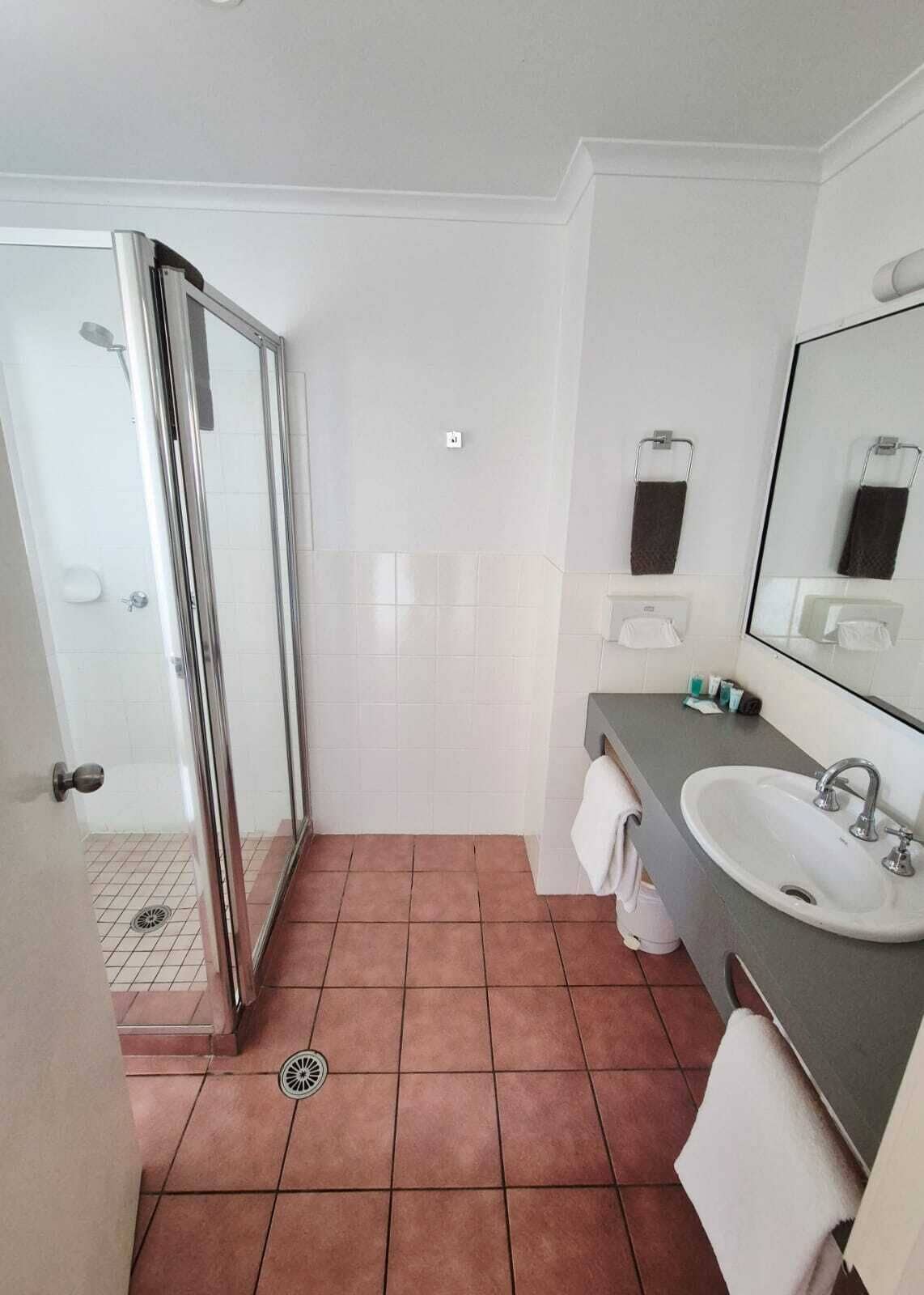 Une salle de bain avec une porte de douche en verre, un lavabo, un miroir et un porte-serviettes.