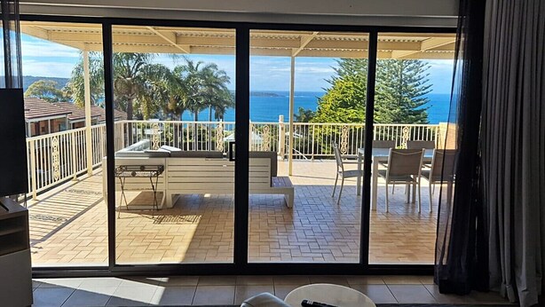 Una habitación con un gran ventanal corredera que da a un patio exterior con vista al océano y palmeras.