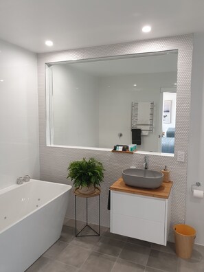A modern bathroom with a large mirror, a freestanding bathtub, a wooden vanity with a sink, and a potted plant.