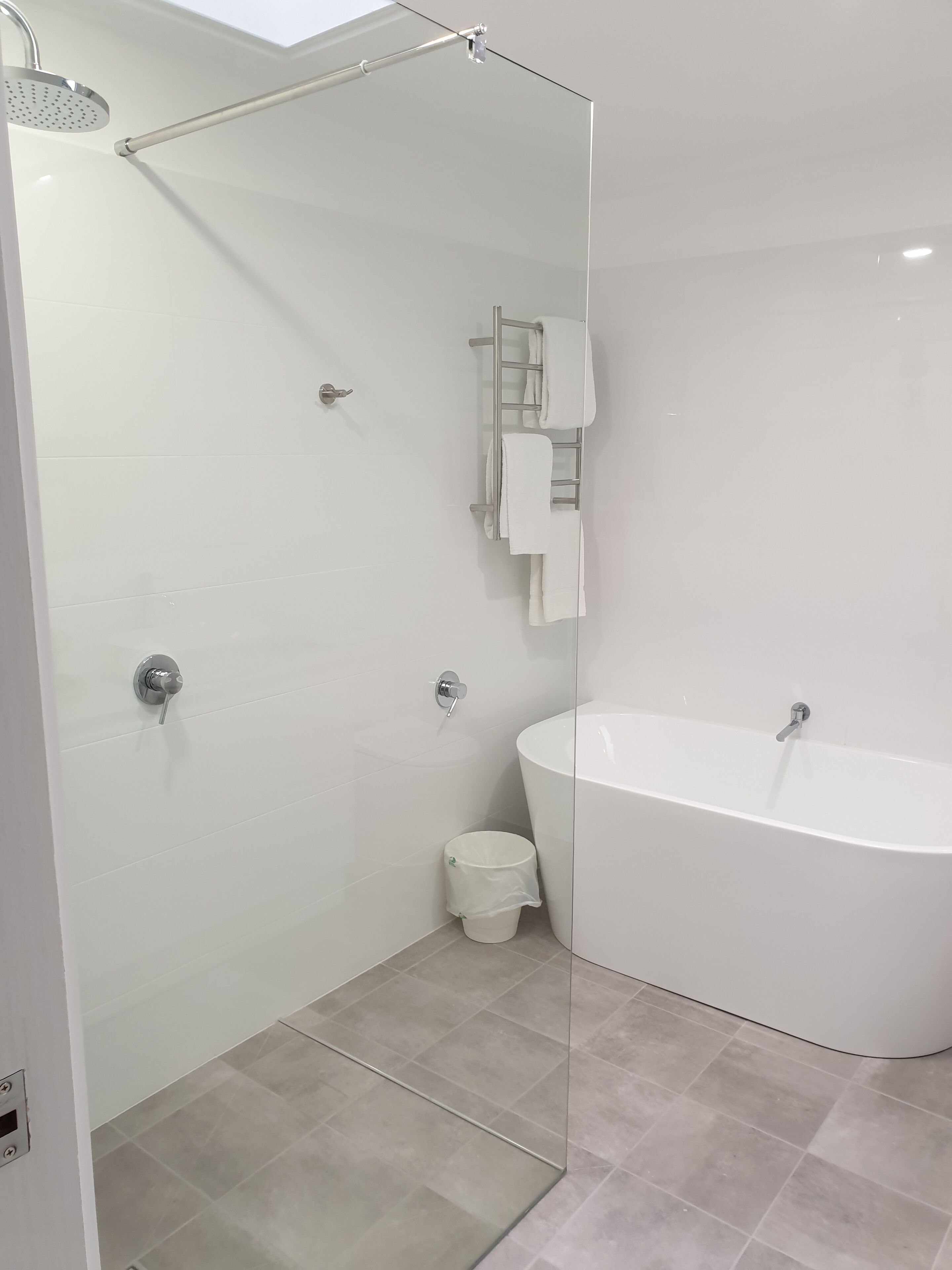 A modern bathroom with a glass-enclosed shower, a freestanding bathtub, and a towel rack.