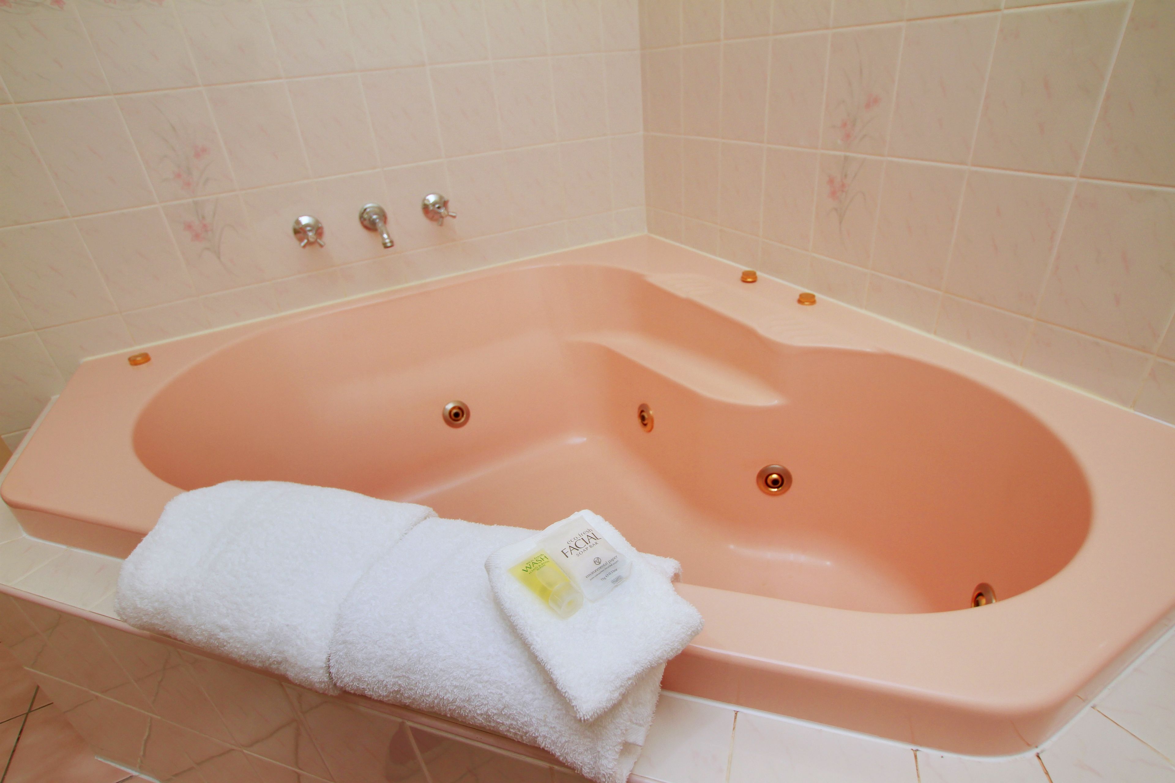 A pink bathtub with a white towel and a bottle of facial cleanser.
