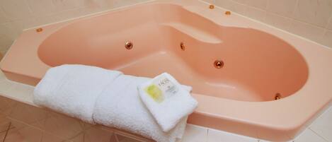 A pink bathtub with a white towel and a bottle of facial cleanser.
